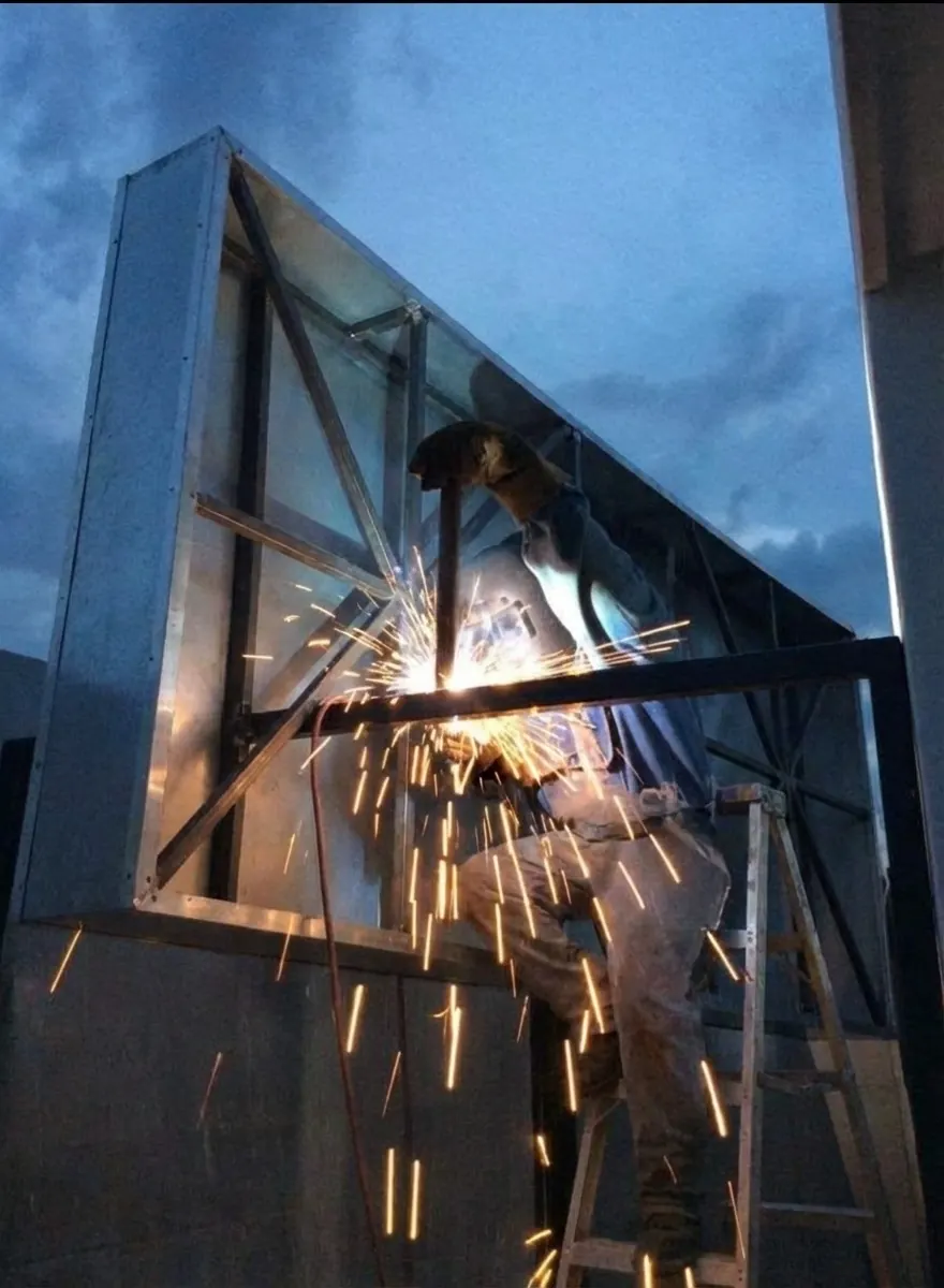 Soldador AVM armando la estructura metálica de un anuncio luminoso de noche, con chispas saltando
