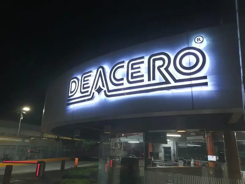 Letras 3D de DEACERO encendidas de noche con halo de luz posterior sobre la fachada curva de su planta